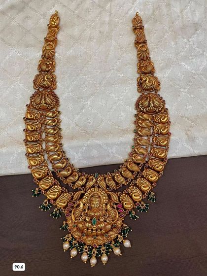 This double-layered temple haram is crafted from 92.5 silver with gold plating. It features intricate peacock and goddess motifs, and is embellished with green stones and pearls.