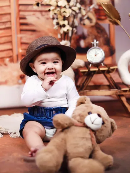 A sweet and smiling portrait of a baby boy in a hat, posing with his teddy bear.