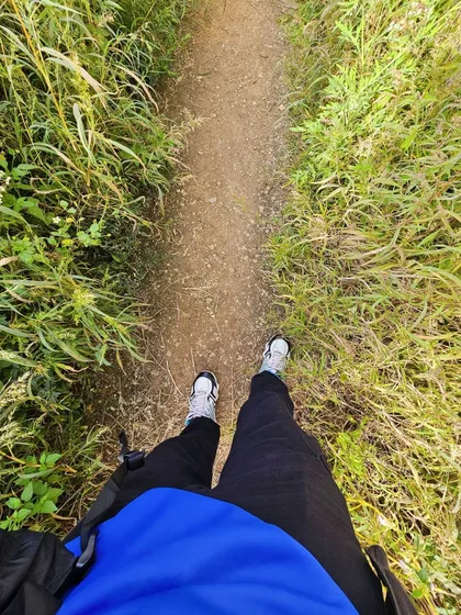 The path to adventure. A first-person view of the trail at Skandagiri, surrounded by tall grass and the promise of a great view ahead.