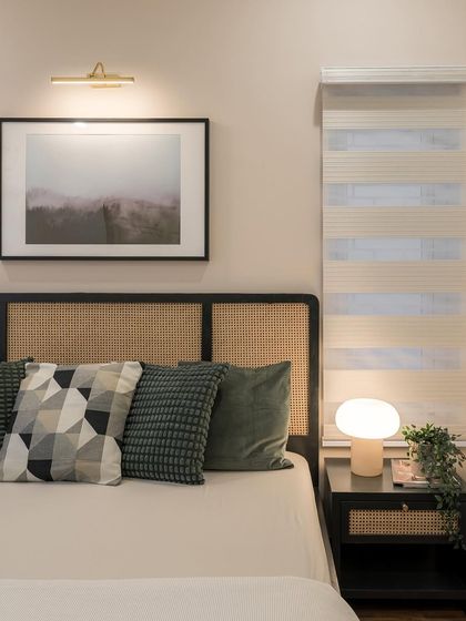 A close-up of a master bedroom headboard, featuring natural cane panels set in a dark wood frame. The mix of textures, from the woven cane to the soft cushions, creates a tactile and inviting atmosphere.