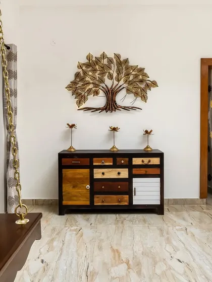 A detail shot of a unique console table made from mismatched drawers, set against a white wall with a decorative metal tree. The indoor swing adds a playful and traditional element to the living space.