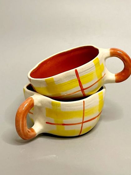 Elevate your morning routine with these handcrafted ceramic mugs. This design features a playful yellow plaid pattern with a vibrant red interior, making it a unique work of art.