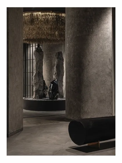 The central rock installation in the 'Frozen' project, viewed through a passage. The interplay of light and shadow on the textured columns creates a sense of depth and mystery, drawing visitors further into the space.