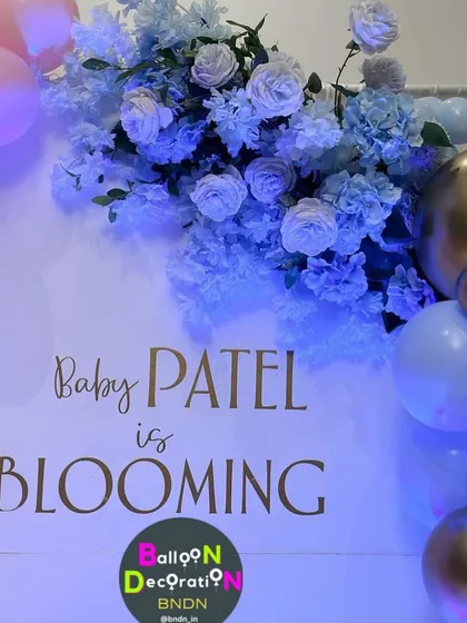 A close-up of the "Baby Patel is Blooming" personalized backdrop, combining elegant script with beautiful blue floral arrangements.