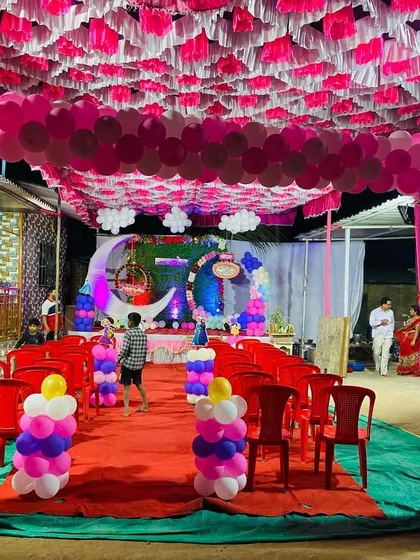 A full view of a naming ceremony pandal, with a long balloon arch running along the ceiling and a decorated stage.