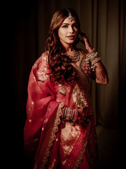 A soft, dreamy, and royal look. The dramatic lighting in this shot creates a painterly effect, highlighting the bride's features and the rich texture of her red outfit.