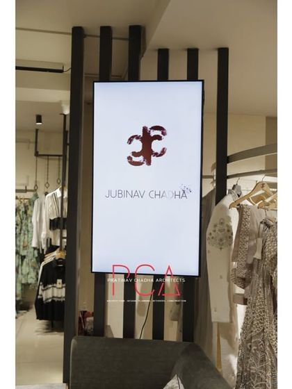 A digital display screen integrated into a slatted wooden partition, used for showcasing the fashion brand's latest work.