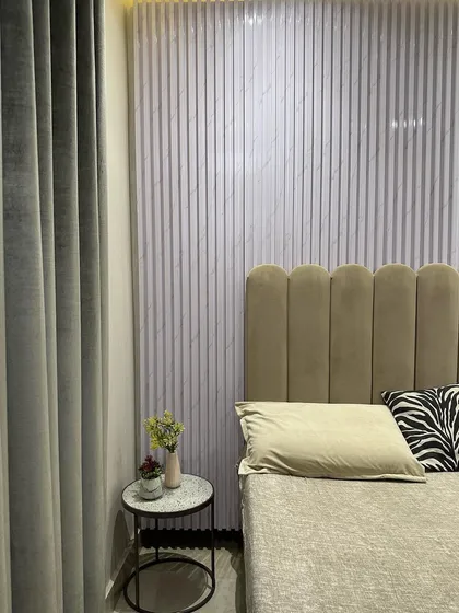 Texture plays a key role in this bedroom design. A fluted panel accent wall creates a subtle yet impactful backdrop for the scalloped, velvet-upholstered headboard. The combination of these elements adds depth and a tactile quality to the room.