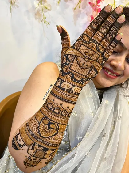 A smiling client with her full-arm bridal mehendi, showcasing a mix of elephants, peacocks, and architectural elements.