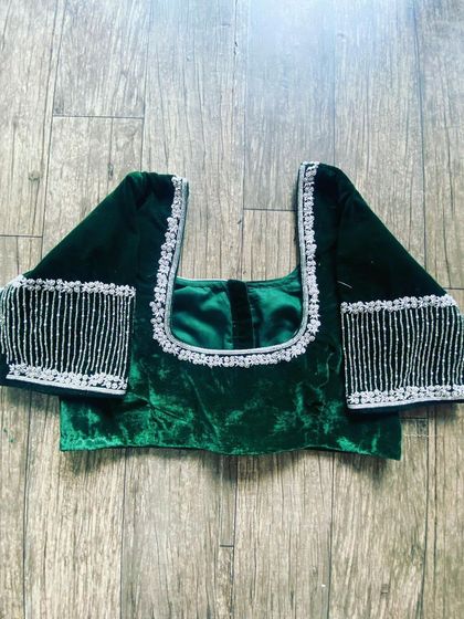 A dark green velvet blouse with a modern design. The sleeves feature hanging beadwork that creates a fringe effect.