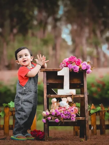 An outdoor first birthday shoot with the little one standing proudly next to a ladder decorated with flowers and a "1".