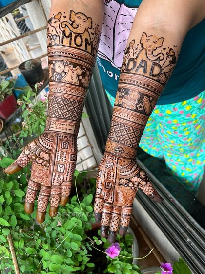A very personal and detailed baby shower mehendi. This design includes "Mom" and "Dad" with cute elephants, baby clothes, and even the due date, creating a beautiful story on the arms.
