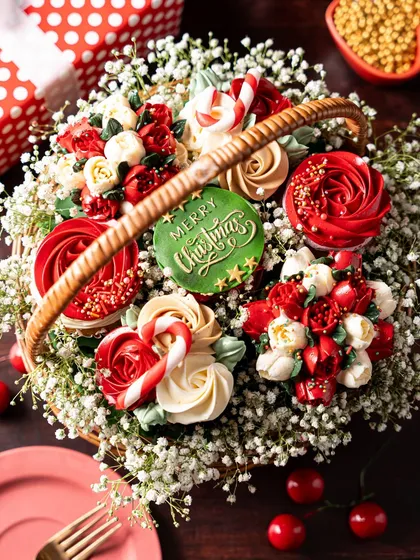 A close-up of the Christmas cupcake bouquet, showing the detailed piping work on the floral-style cupcakes and a "Merry Christmas" plaque. This edible arrangement is a showstopper gift for the holidays.