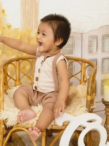 A happy baby boy points with excitement while sitting in a wicker chair during his photoshoot.