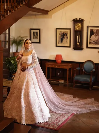 A bride stands in her magnificent pale pink lehenga, its long train flowing behind her, inside a vintage, wood-paneled hall. This full-length bridal portrait is all about capturing the elegance and detail of the bride's final look.