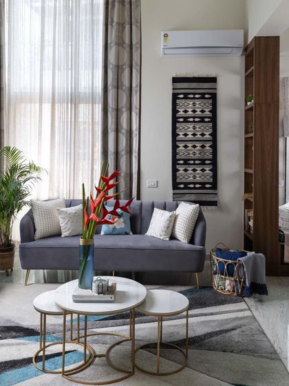 A contemporary living room designed for comfort. The space features a sleek grey sofa, nested marble coffee tables, and a mix of textures from the rug and wall hanging, creating a relaxed yet stylish family area.