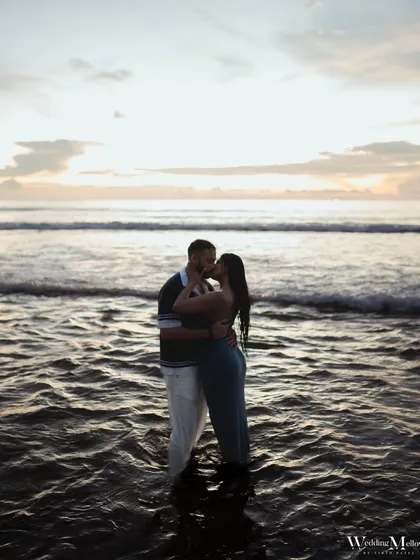A romantic kiss in the waves as the sun sets over Phuket. This wide shot captures the beautiful seascape and the intimacy of the couple, creating a classic destination pre-wedding photograph.