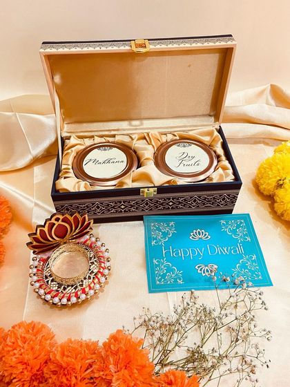 A luxurious wooden box containing two ornate jars for makhana and dry fruits. Paired with a decorative lotus T-light holder, this makes for a royal Diwali gift.