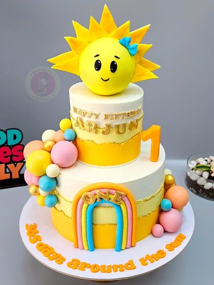 A "365 days around the sun" themed cake for Arjun's first birthday, with a bright, happy sun topper and a rainbow.