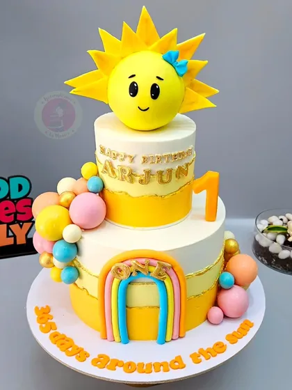A "365 days around the sun" themed cake for Arjun's first birthday, with a bright, happy sun topper and a rainbow.
