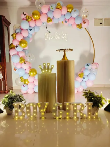 A classic gender reveal setup with a pink and blue balloon arch on a gold ring, an 'Oh Baby' neon sign, and 'BOY GIRL' marquee letters.