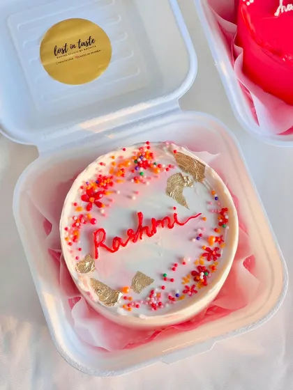 A close-up of the personalized "Rashmi" bento cake from the set, featuring colorful sprinkles and gold leaf for a celebratory touch.