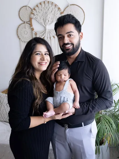 A happy family portrait with their newborn. The parents are looking at the camera, proudly presenting their new baby, who is nestled safely in their hands.