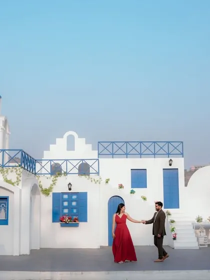 A grand, cinematic shot at a Santorini-inspired location in Pune. The sweeping view of the white and blue architecture creates a breathtaking backdrop for a romantic pre-wedding photo.