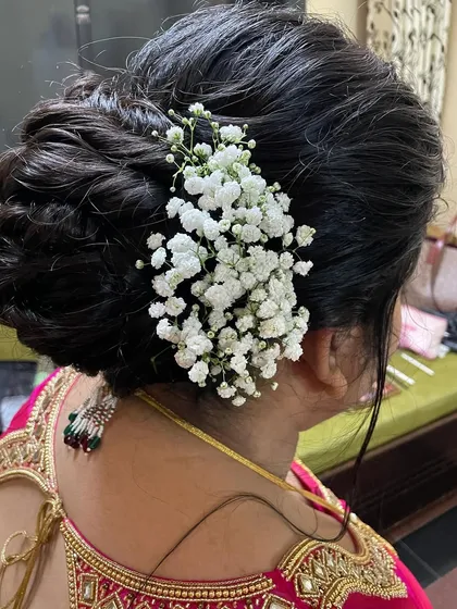 A simple and elegant bridal bun adorned with a sprig of fresh baby's breath (gajra). This is a timeless hairstyle that works beautifully with any traditional outfit.