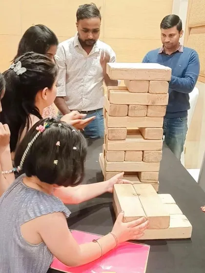 Guests gathered around a table playing Giant Jenga indoors at a birthday party. This game is versatile and can be set up in almost any event space.