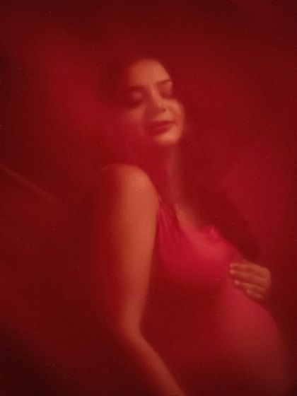 Bathed in crimson. This artistic, moody portrait uses a sheer red fabric to create a soft, dreamlike effect. It’s a poetic and emotional interpretation of the maternity journey.