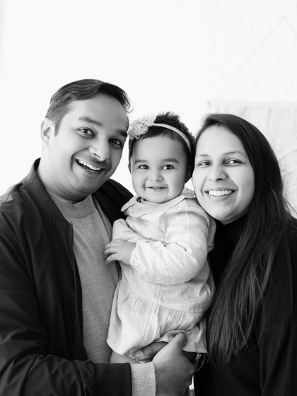 A classic black and white family portrait with both parents and their baby smiling together.