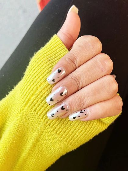 A cute and simple design with tiny, hand-painted black hearts scattered over a pearly white base on long, square-shaped nails.