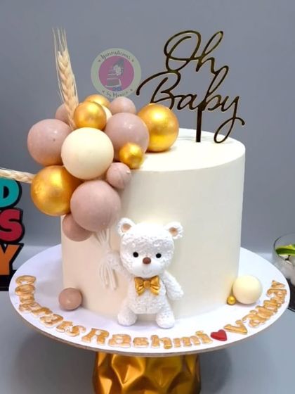 A chic and modern baby shower cake in neutral tones, featuring a textured teddy bear and a cascade of edible chocolate spheres.