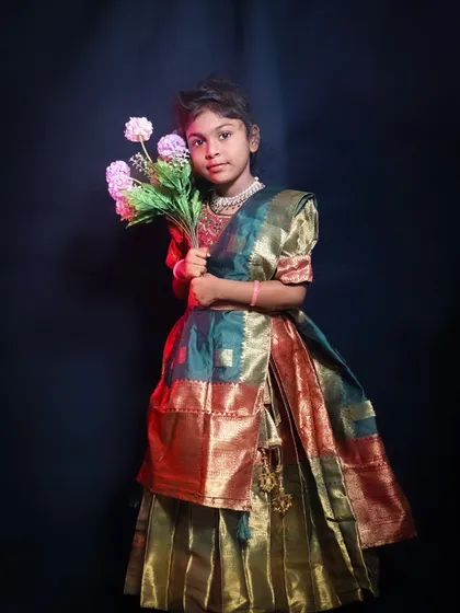 A dramatic studio portrait with a touch of cinematic flair. The lighting and smoke effect create a moody atmosphere as this young girl in traditional dress holds a bouquet of flowers.