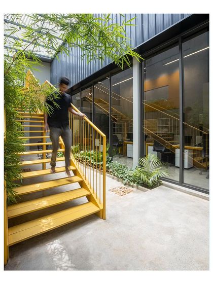 The bright yellow staircase is a central design feature, adding a pop of color and energy to the office. It connects the floors while acting as a sculptural element within the courtyard space.
