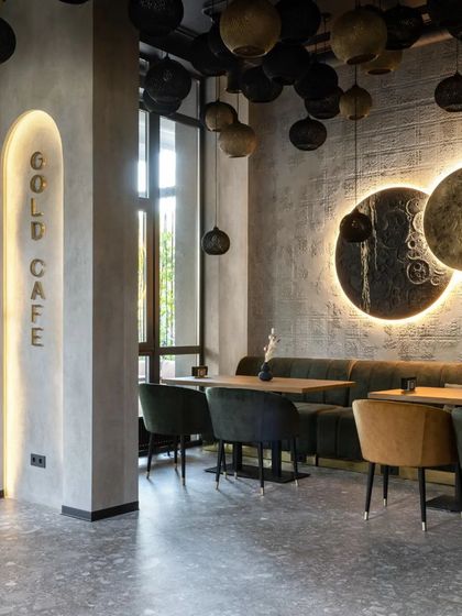 The "Gold Cafe" interior uses a sophisticated palette of grey, black, and gold. The backlit wall art and signage create a warm glow against the textured concrete walls.