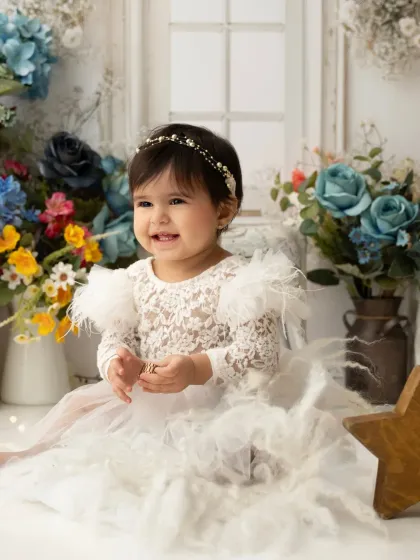 A happy baby girl in a white feathered dress, laughing during her floral-themed milestone session.