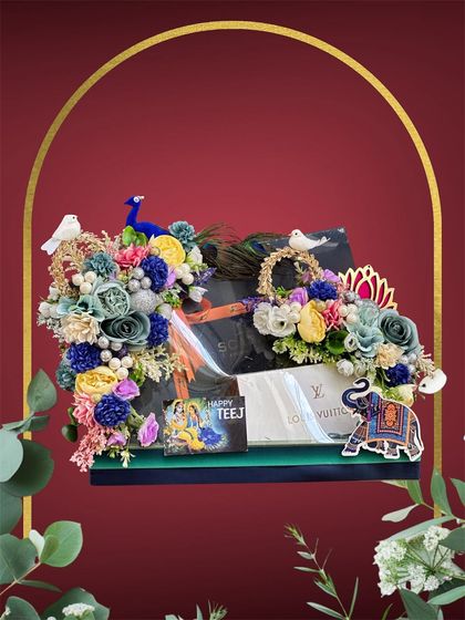 This Teej hamper includes a mix of designer items and traditional elements. The arrangement is brought to life with a colourful assortment of flowers, a peacock figurine, and an elephant motif.