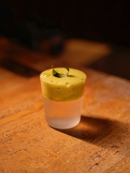 A detailed look at the layered Neer More 2.0, showcasing its vibrant green chili and coriander foam top. It's a drink that's as visually striking as it is flavourful.