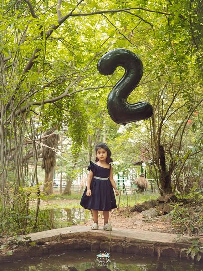 This wide shot captures the beautiful, lush environment of the park, making the little girl and her balloon the focal point of a grand scene.