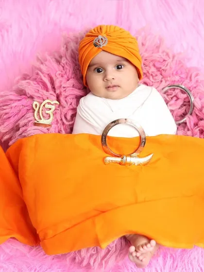 This little one looks so serene and alert in his orange turban. The setup includes symbolic elements against a soft pink backdrop, creating a unique and memorable portrait.