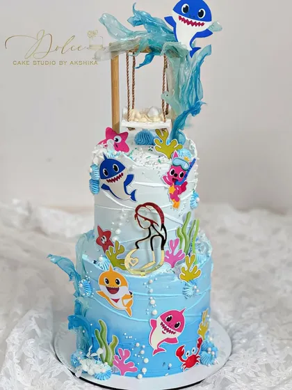A fun twist on our swing cake, this one is for a "Baby Shark" themed baby shower. The two-tiered cake is decorated with characters from the show and underwater details.