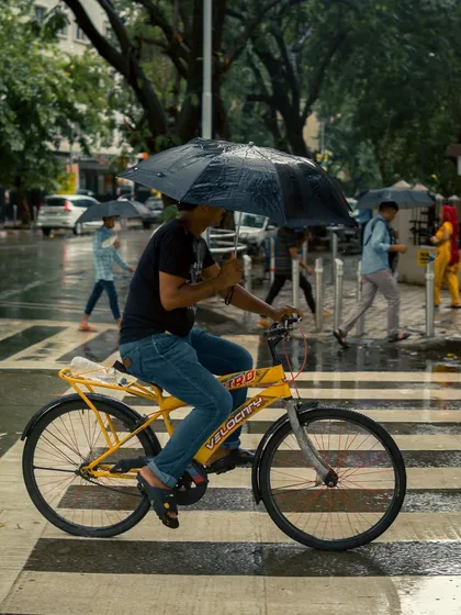 A man on a yellow bicycle holds an umbrella while crossing the street. The photo captures a moment of balance and everyday hustle, with the yellow of the bike adding a vibrant touch.