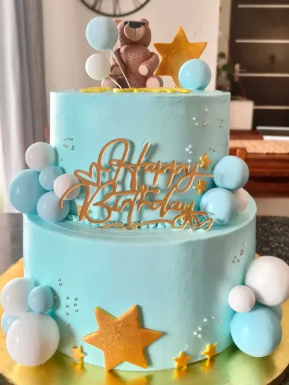 A lovely two-tier teddy bear cake in pastel blue, decorated with stars and balloon clusters. A classic theme for a young child's birthday.