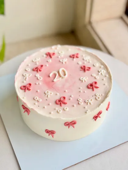 A full view of the delicate 20th birthday cake, with its soft blush center and tiny red and white bows piped around the top and sides.