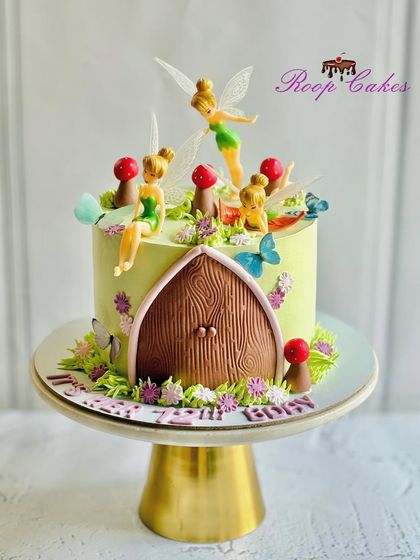 An enchanted fairy garden cake. This design features a fairy door, toadstools, flowers, and several tiny fairies, including Tinkerbell, creating a magical world.