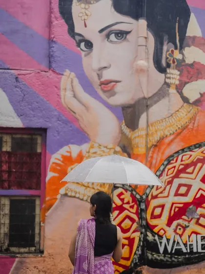 A unique composition blending street art with portraiture. The model, seen from behind with an umbrella, stands before a large, colorful mural of a woman, creating a powerful dialogue between art and life.