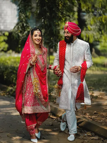 Walking together into their future. This shot captures the couple in a moment of shared happiness, showcasing the bride's stunning red salwar kameez and the groom's elegant sherwani.