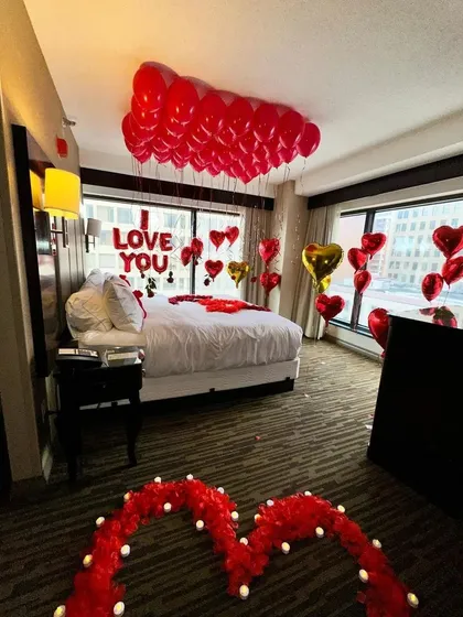 This wider view shows how a full room decoration can completely transform a space. The heart-shaped path of rose petals on the floor leads to the beautifully decorated bed, creating a complete experience.